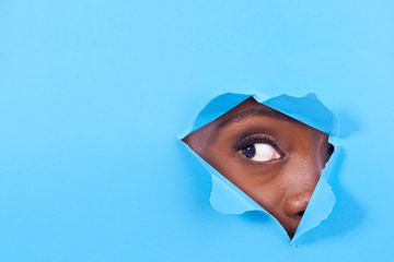 An eye peeking through torn blue paper