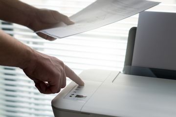 Someone holding papers and pressing a button on a printer.