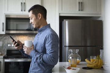 A man looking at his phone while holding a cup of coffee in his other hand