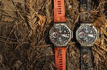 Two Amazfit T-Rex 3 smartwatches against a muddy background of pine needles.