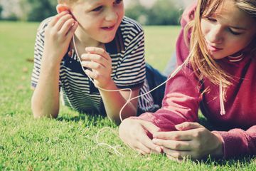 Two children lying on grass listening to music through a smartphone