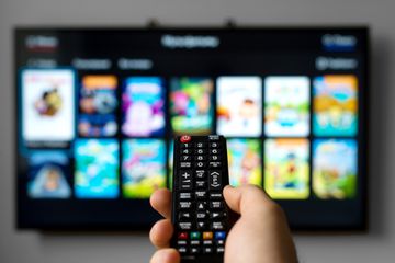 A hand holding a remote control and pointing it at a smart TV.