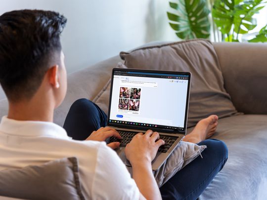 A man sitting on a couch with his legs crossed and a laptop on his lap using Bing AI in Google Chrome.