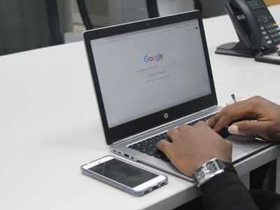 Person on laptop using Google next to mobile and landline phones