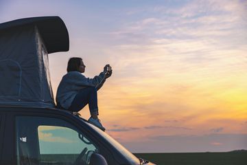 A woman sitting on the roof a camper van holding her smartphone 