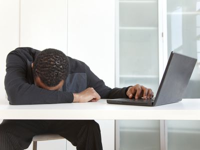 Businessperson with head on desk frustrated with popup ads on a laptop