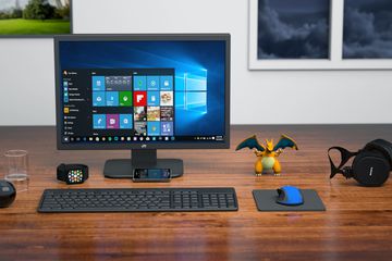 Windows 10 computer monitor with keyboard, mouse, headphones, and small dragon action figure on a desk.