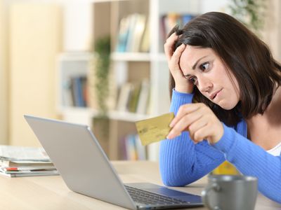 A worried woman holding her credit card and looking at a laptop