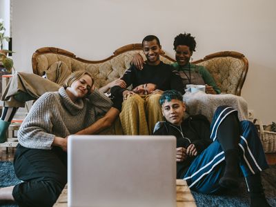 A group of people in a living room, watching a laptop