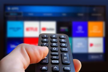 A man is holding a remote control of a smart TV in his hand