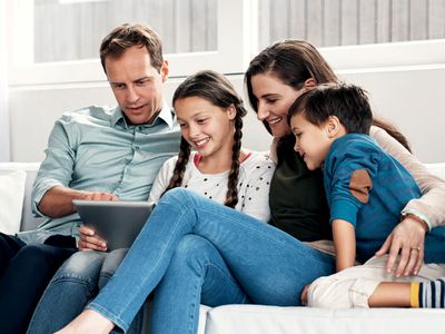 A father, mother, son, and daughter sitting on a sofa looking at data on an iPad.