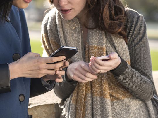 Two women looking secretive at Snapchat on their iPhone smartphones.