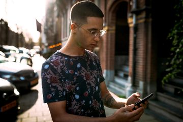 A young male adult with glasses holding an Android smartphone.