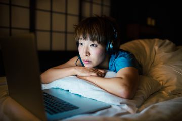 Someone streaming a movie while wearing headphones in the bed at night.