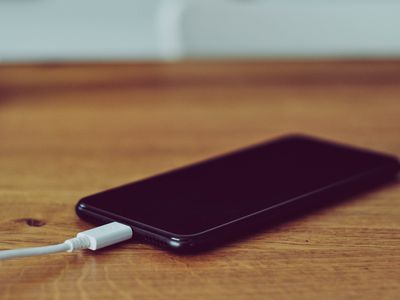 iPhone plugged into charging cable, resting on a brown wooden desk