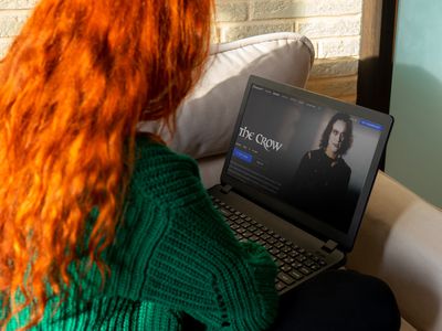 A woman with red hair and a green sweater watching The Crow movie on her laptop.