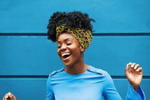 Joyous Black woman, dressed in blue, singing in front of blue wall