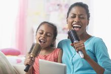 Hispanic mother and daughter singing with hairbrushes and digital tablet