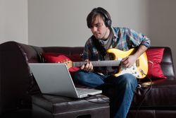 Man playing guitar wile looking at laptop