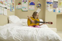 Girl (5-7) sitting on bed playing acoustic guitar