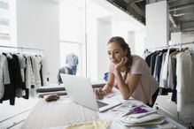 Fashion designer on computer surrounded by clothes