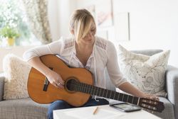 Woman sitting on sofa and playing acoustic guitar