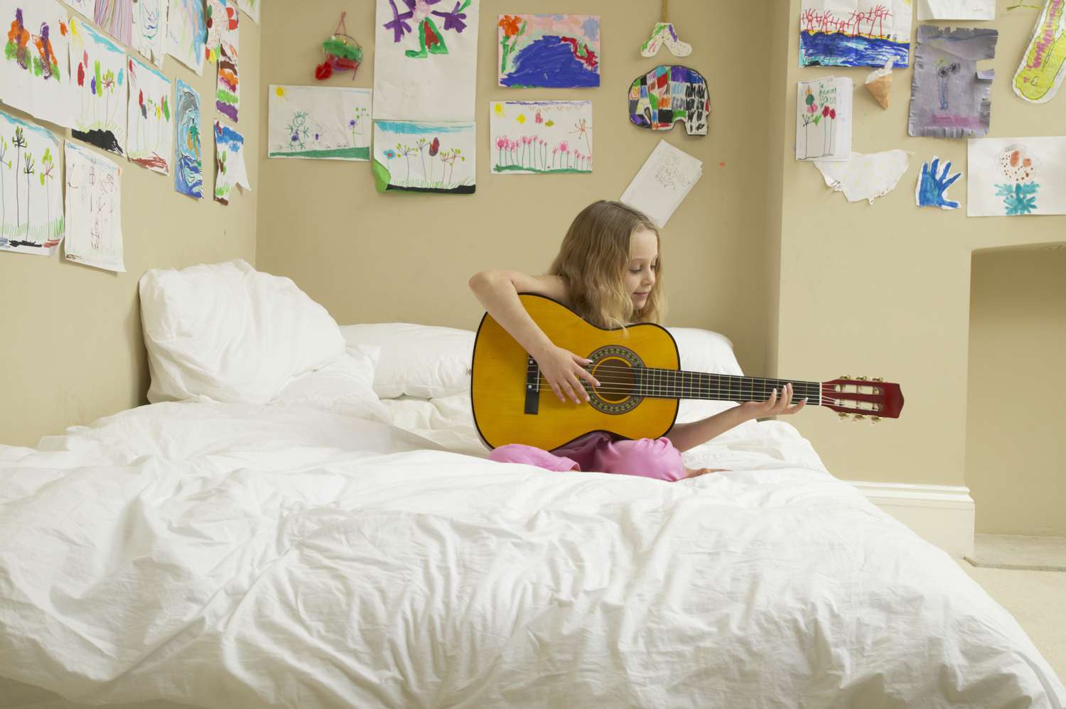 Girl (5-7) sitting on bed playing acoustic guitar