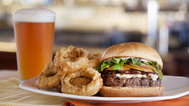 Burger with onion rings on plate beside pint of beer