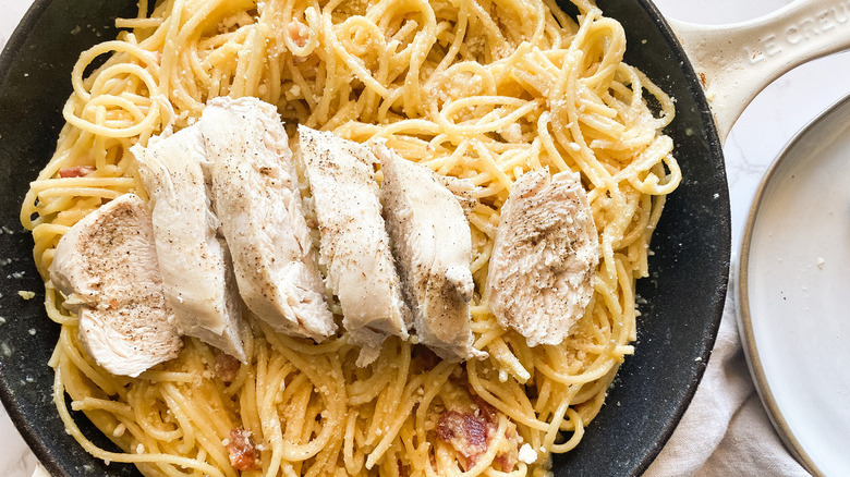 Carbonara topped with cooked chicken breasts in a skillet.