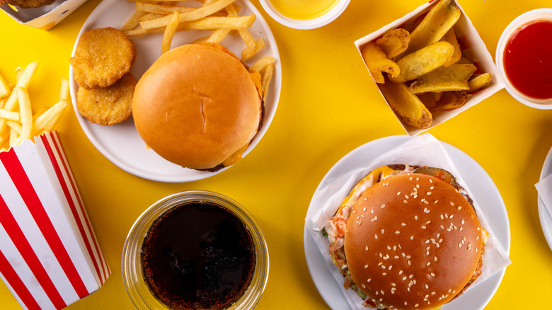 overhead shot of fast food burgers, French fries, and chicken nuggets on yellow background