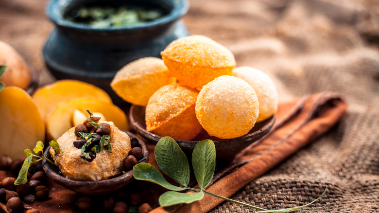 Dish of pani puri pastries alongside fruit and herbal ingredients