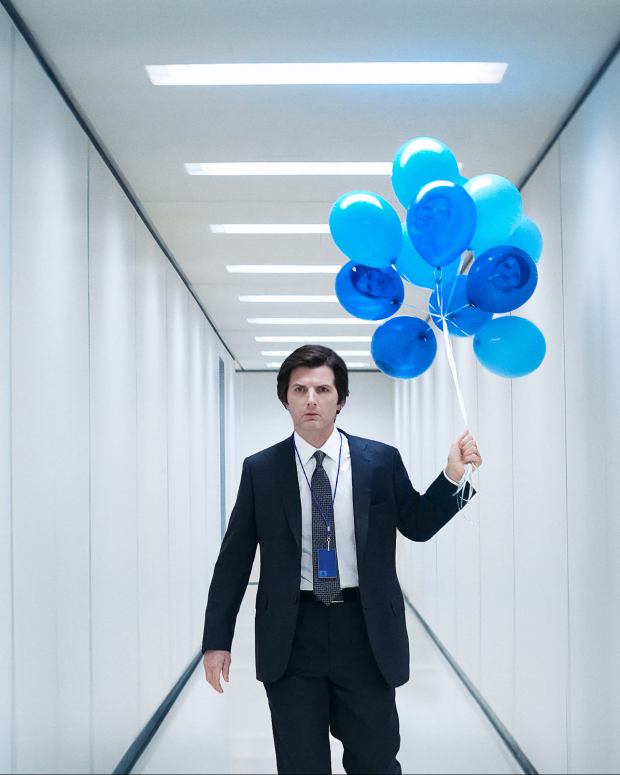 Adam Scott with blue balloons walking down a hall in Severance