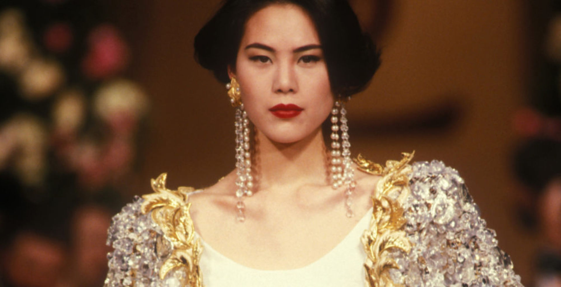 Model wearing a white silky outfit and a silver and gold embroidered jacket designed by Yves Saint Laurent