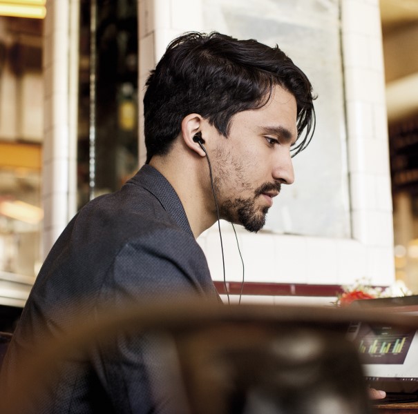 Man using ear buds at a desk, looking downward.