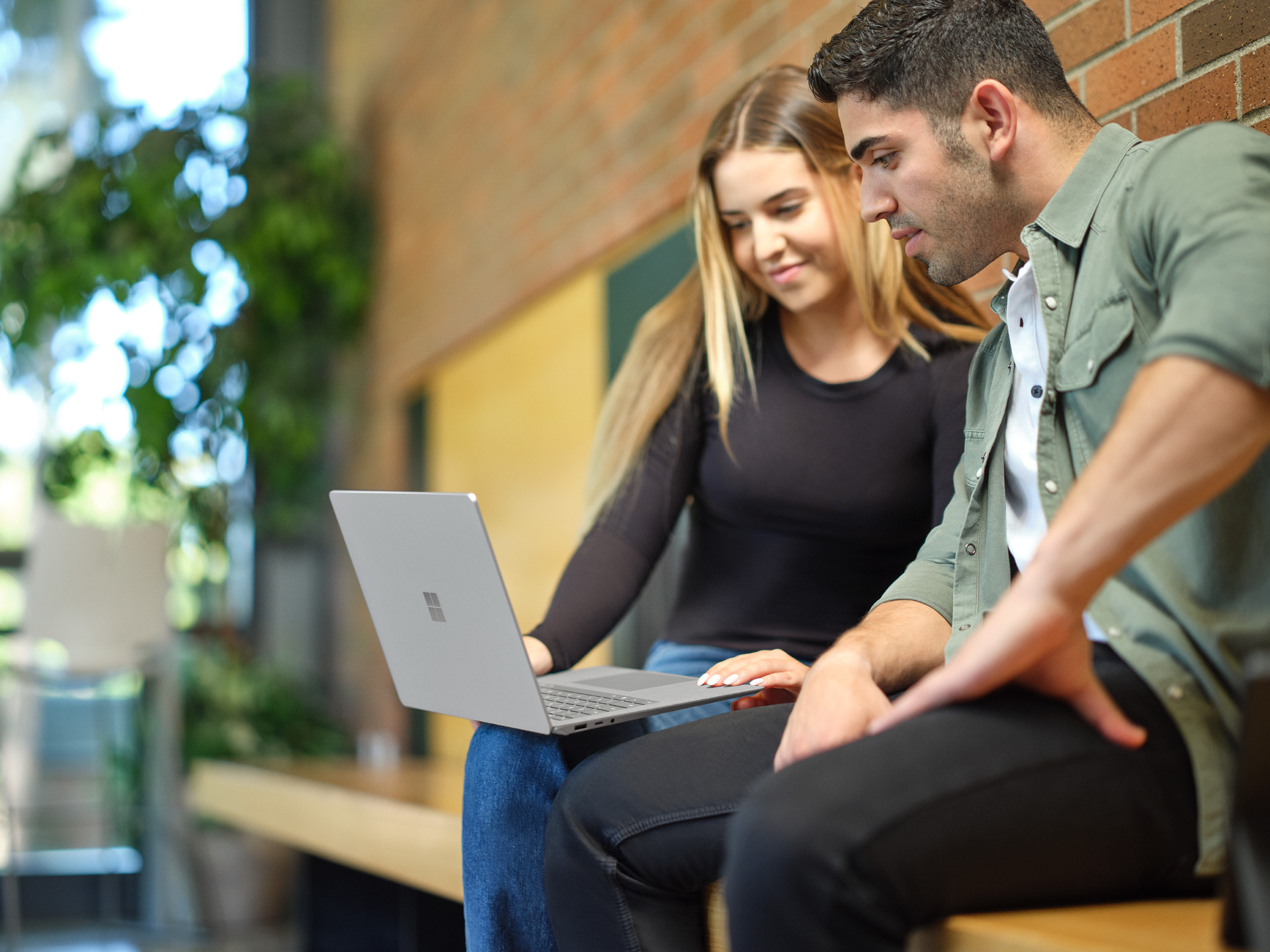 Two people sitting on a bench looking at a laptop together.