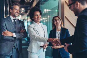 Four business people smiling, two of which shaking hands.