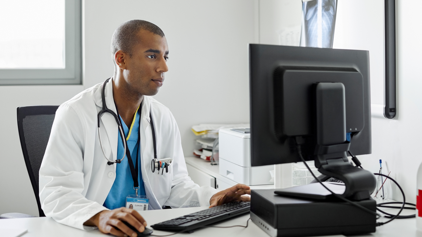 Male Doctor Using Computer At Desk In Hospital