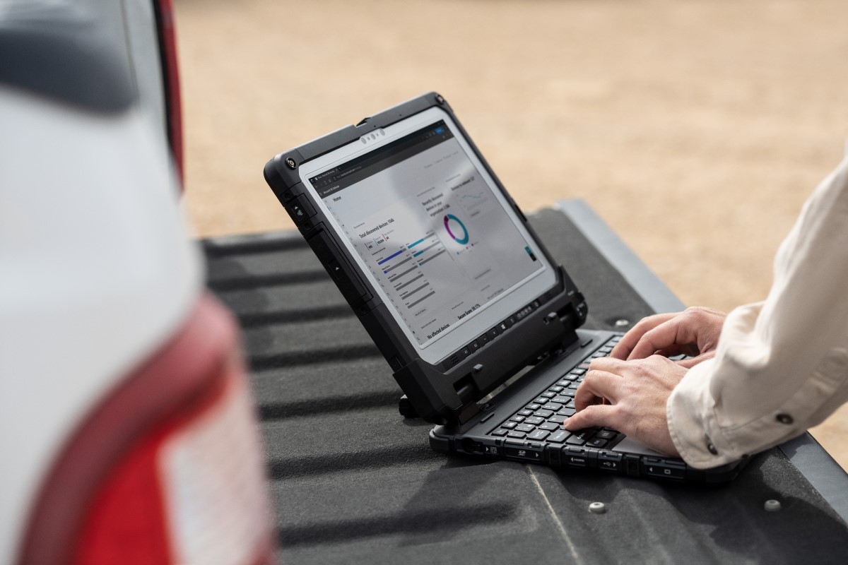 Field engineer using a laptop on truck tailgate to review data after inspection of turbines on a wind farm.