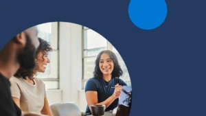 A diverse group of coworkers collaborate in an office space while one takes notes on his laptop.