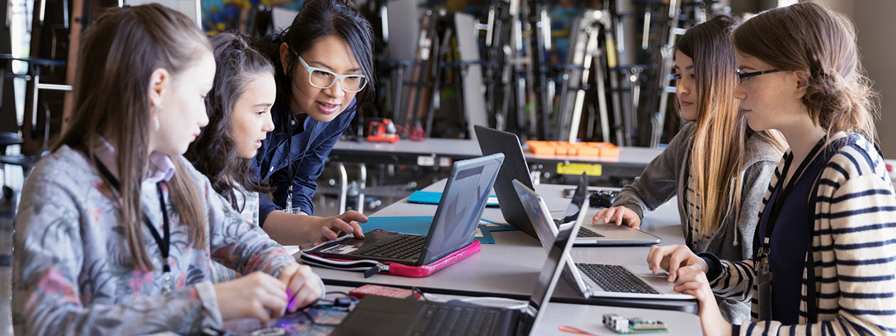 Female teacher with a group of young girls working on their computers