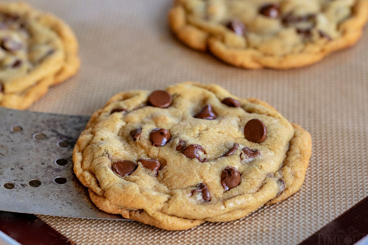 chocolate chip cookie being removed from silicone baking mat with metal spatula