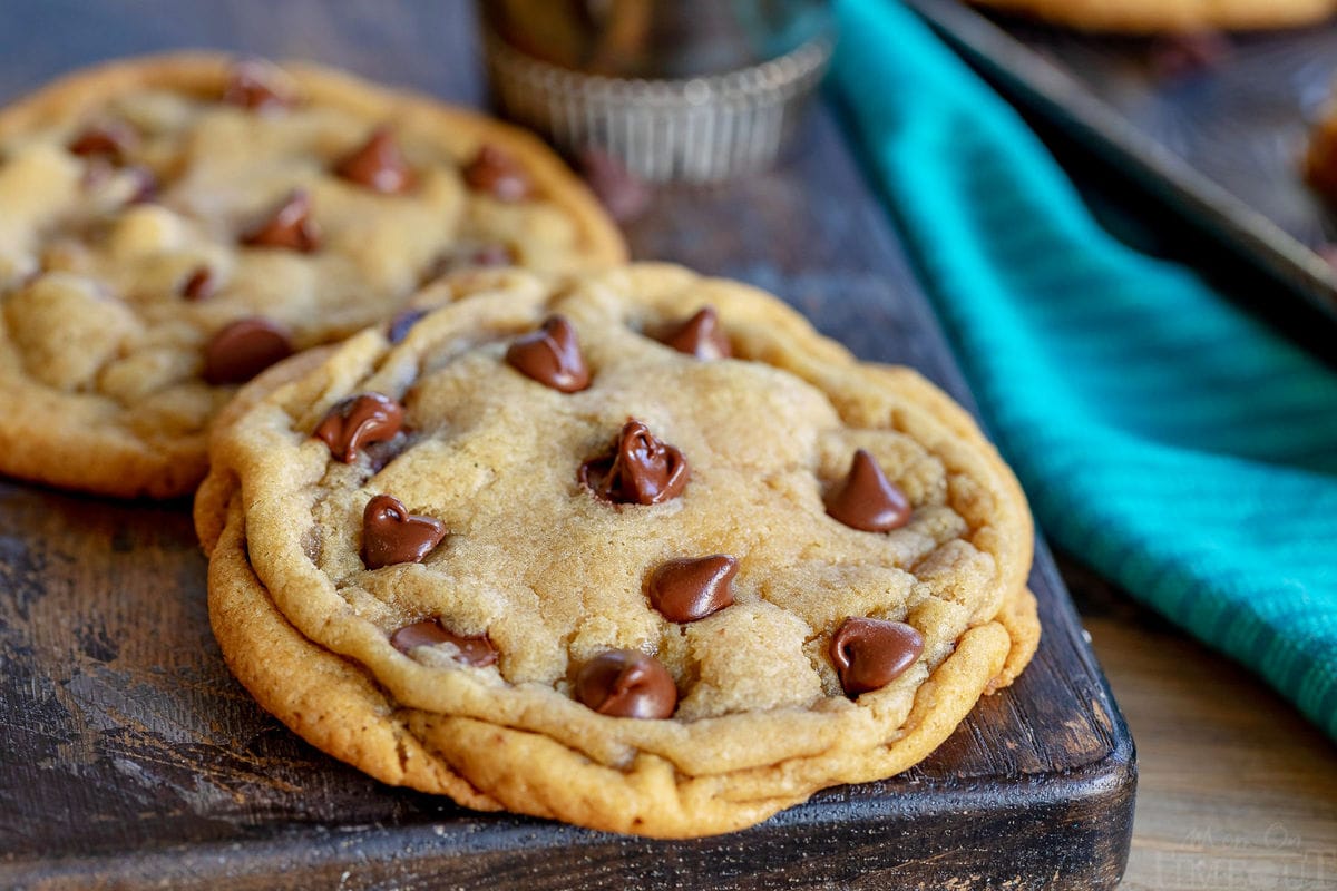 two chocolate chip cookies on dark cutting board with teal napkin on the right