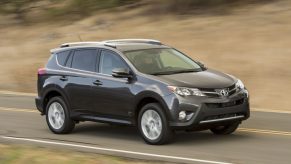 A grey 2015 Toyota RAV4 driving on a two-lane road in right profile angle view