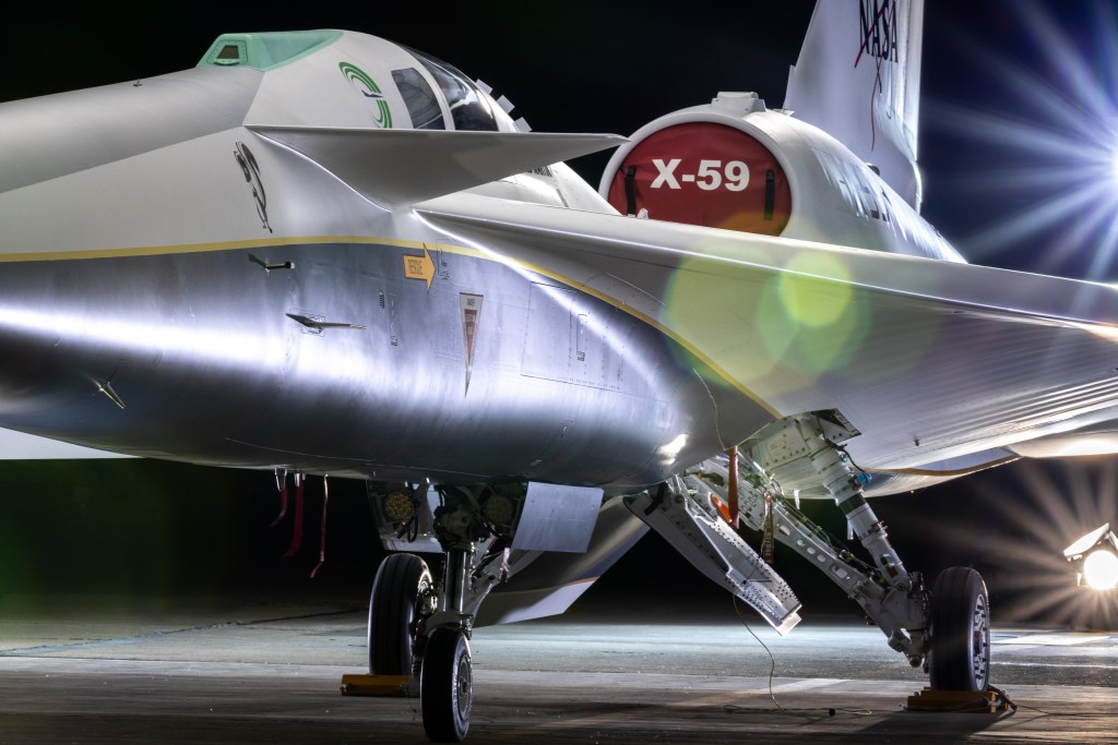 NASA's X-59 airplane sits in its hangar with lights shining on it.