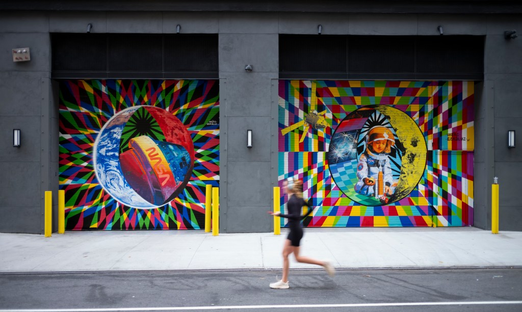 An image of two murals painted on loading dock garage doors. The murals include bold, bright colors and geometric shapes. The image two the left features planet Earth with a satellite that features the NASA logo. The mural on the right has an image of a child in an astronaut suit playing with toys.