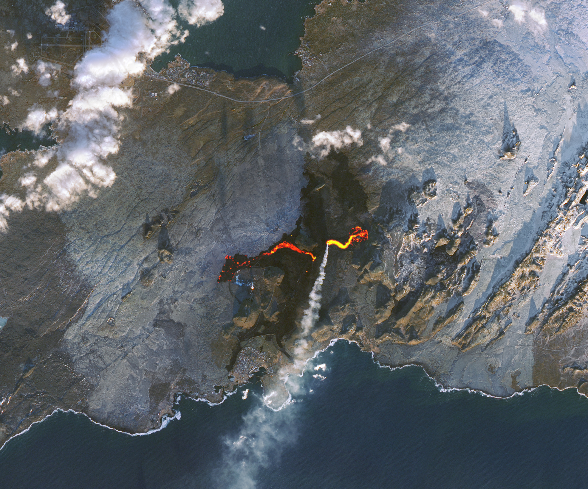 Lava cuts a jagged orange gash across a grayish landscape in this satellite view of Iceland's Reykjanes peninsula on Nov. 24, 2024. A plume of white smoke - gas - streams toward the bottom of the picture.