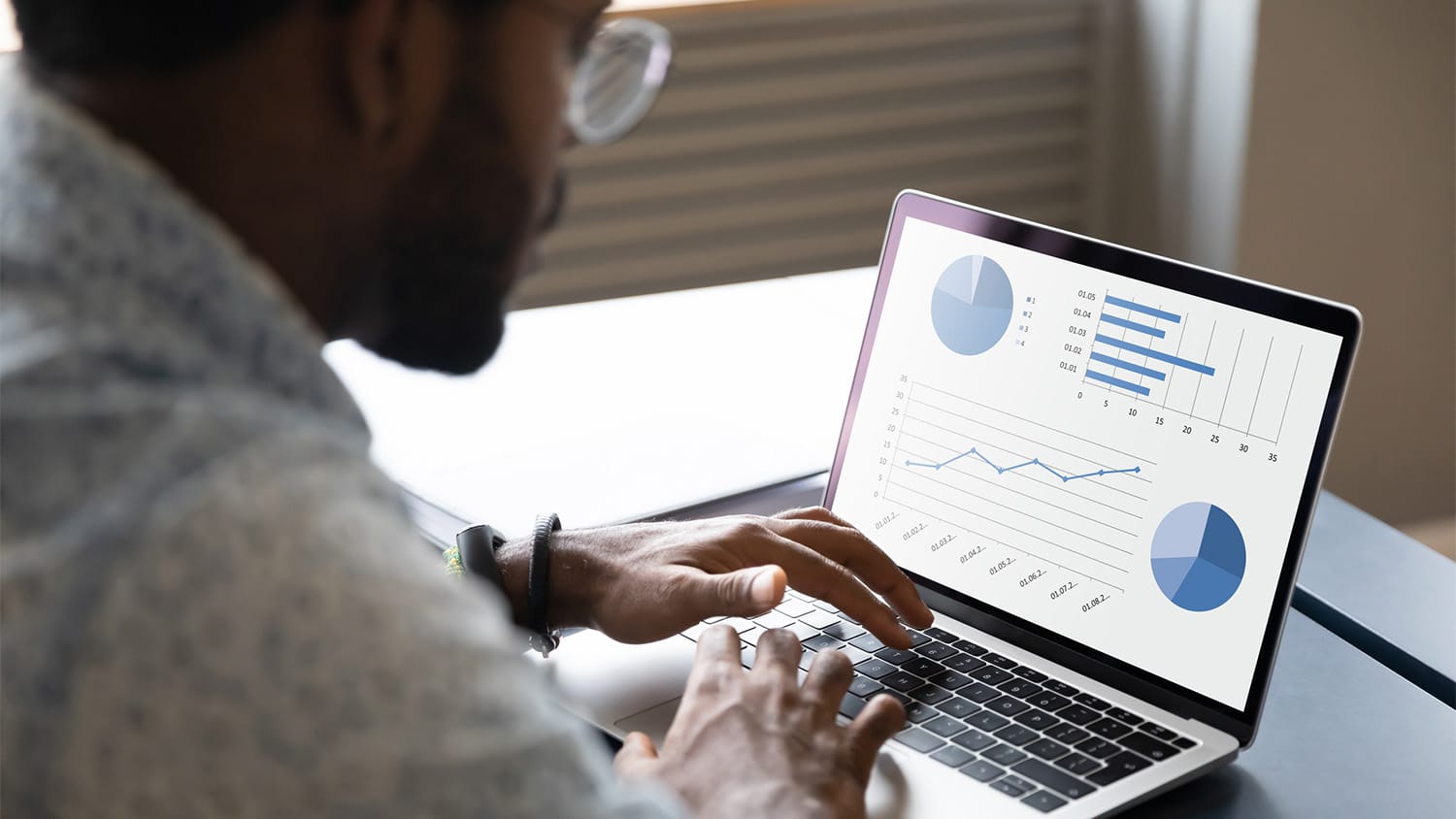 A man in glasses looks at statistical information on his laptop.