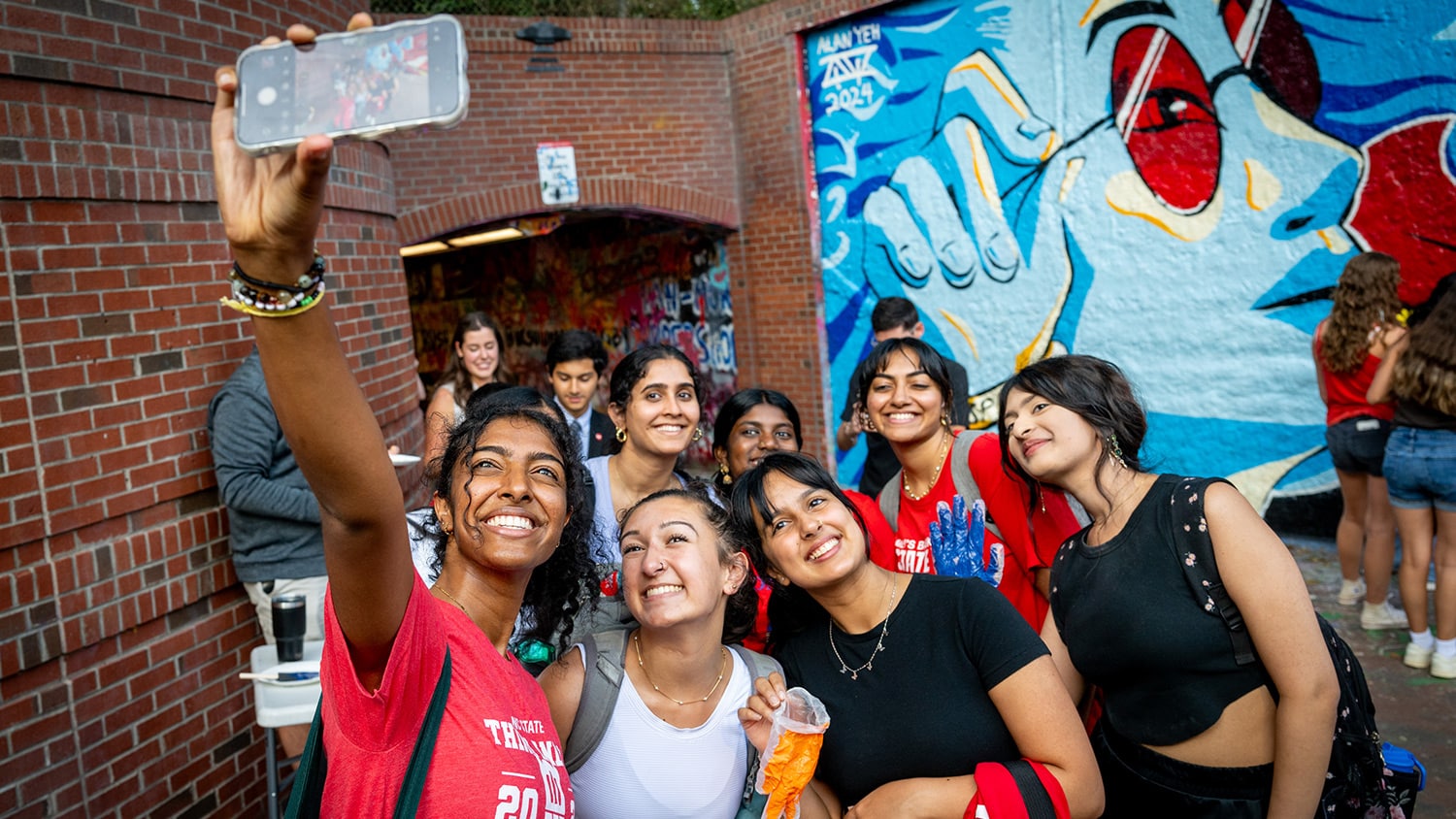 A group of students take a selfie near a colorful mural in the Free Expression Tunnel.