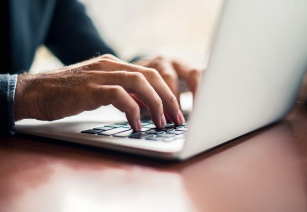 Close up of mans hands typing on a laptop keyboard.