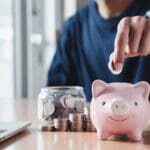 Hand putting coins in a piggy bank for save money and Saving Money concept.